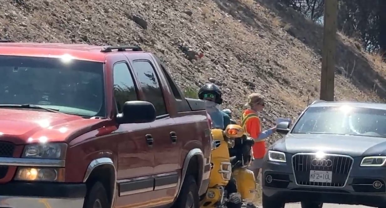Person in a high-visibility vest speaking to a driver in a car lineup near Quilpituk Creek fire area